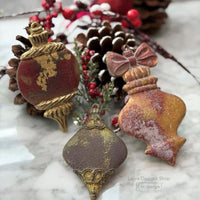 Decorative Christmas ornaments on a marble surface with pine cones and berries. Christmas Ornament mould set shown with the blank mold on the left and the cast  ornament pieces on the right. Winter Luxe Blanks Mould by Redesign with Prima