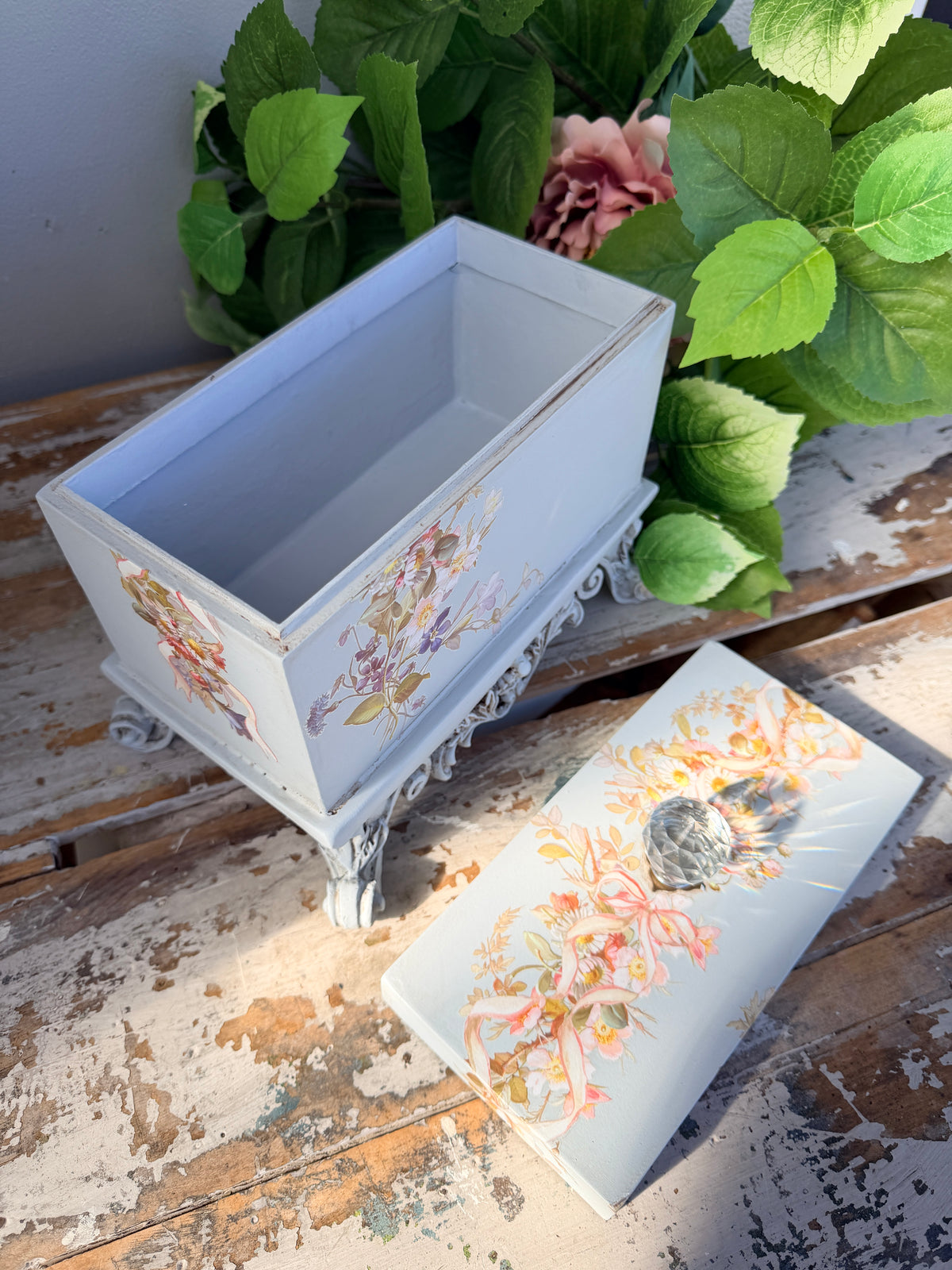 Decorative box with floral and bird design on a stand with greenery in the background. Filigree Blue Lidded Box