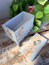 Decorative box with floral and bird design on a stand with greenery in the background. Filigree Blue Lidded Box