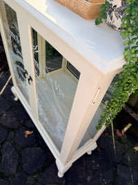 Cabinet with glass doors featuring embossed designs and text. Limestone Cream & White mirrored Display Cabinet with glass shelves
