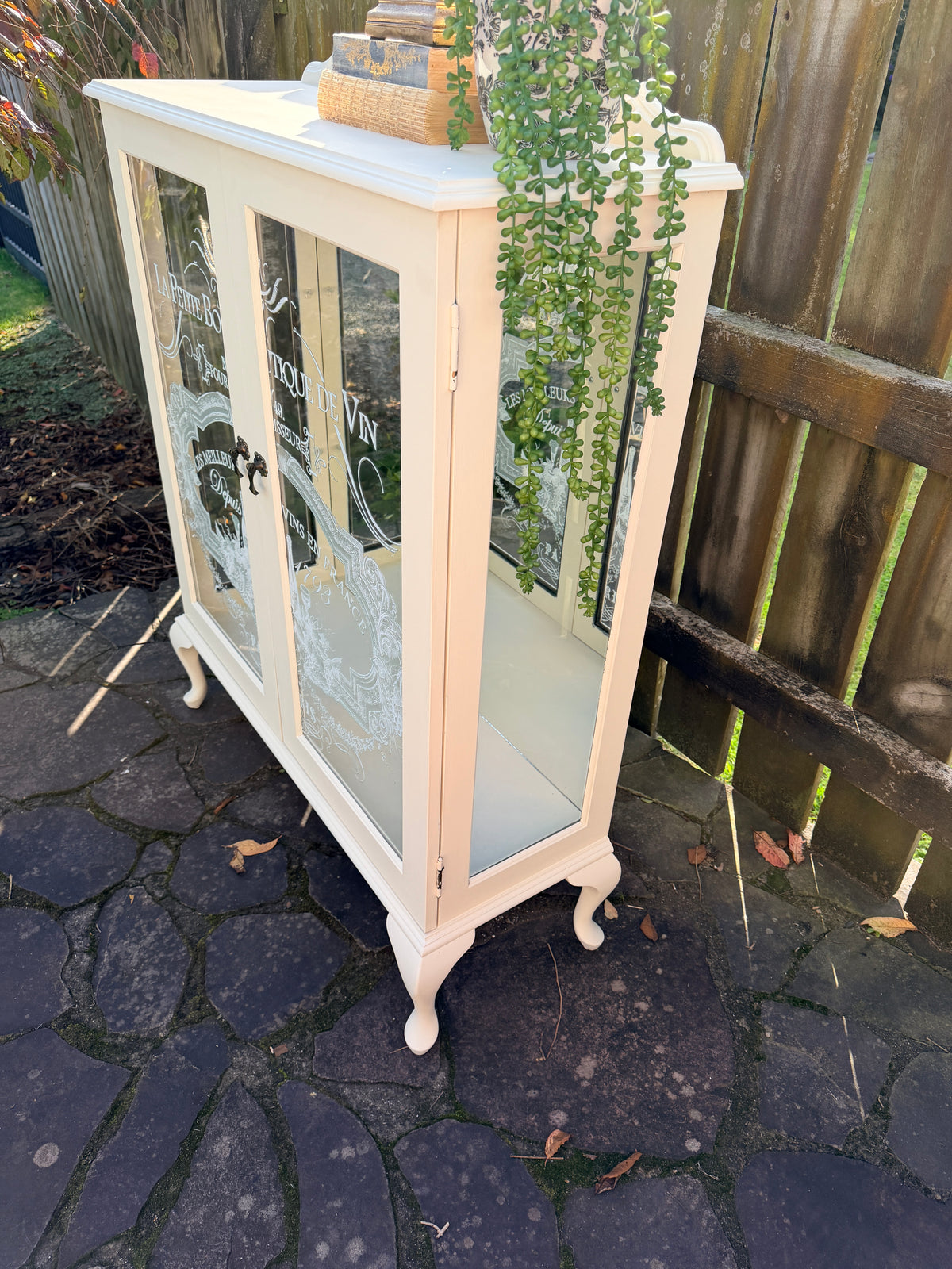 Cabinet with glass doors featuring embossed designs and text. Limestone Cream & White mirrored Display Cabinet with glass shelves
