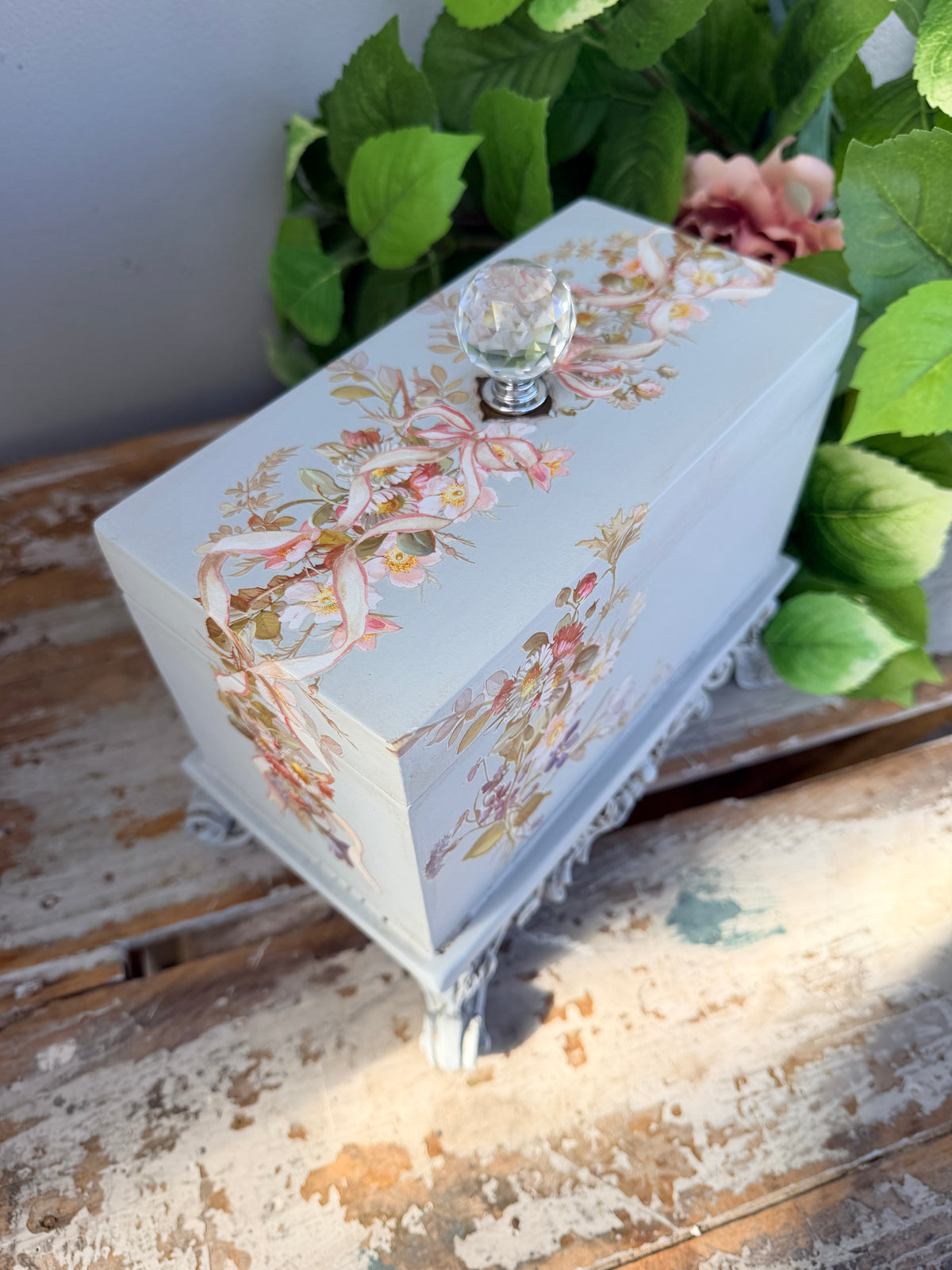 Decorative box with floral and bird design on a stand with greenery in the background. Filigree Blue Lidded Box