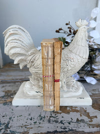 A pair of distressed white rooster bookends holding two vintage-style tan books tied with red string, French Rooster white Book Ends set of 2