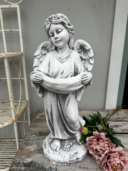 Statue of an angel with wings spread on a wooden surface with flowers. Girl Angel Statue with swag 