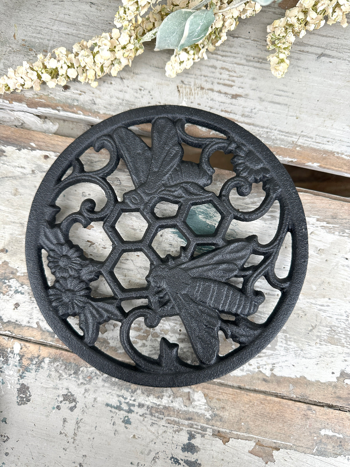 Decorative black metal trivet with bee and honeycomb design on a wooden surface.