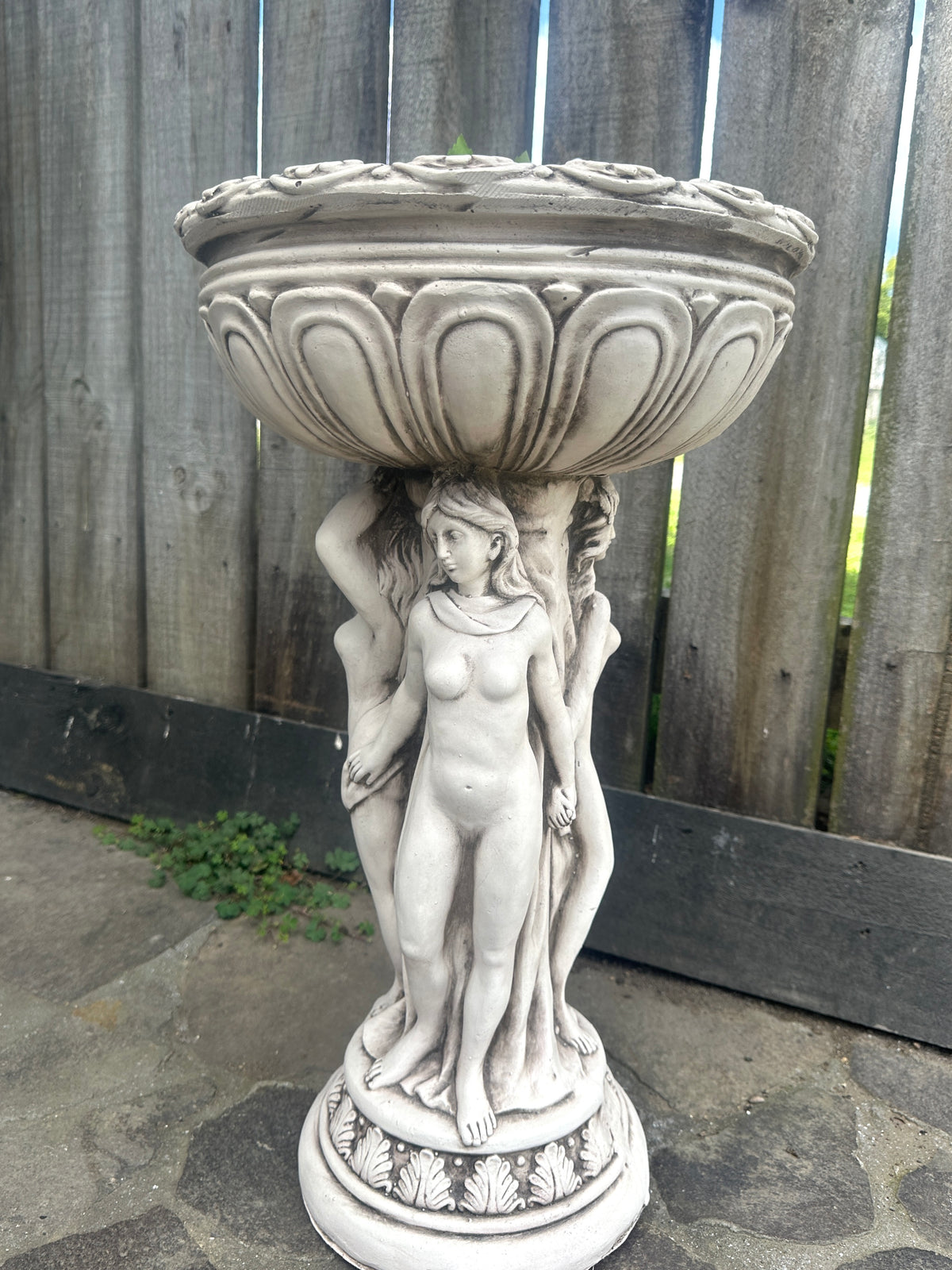 Decorative stone planter with classical design against a wooden fence. Goddess Statue