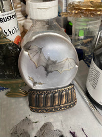 Decorative bottle with a bat design inside a crystal ball on a cluttered surface. Glitter and Glow Mould by Redesign with Prima