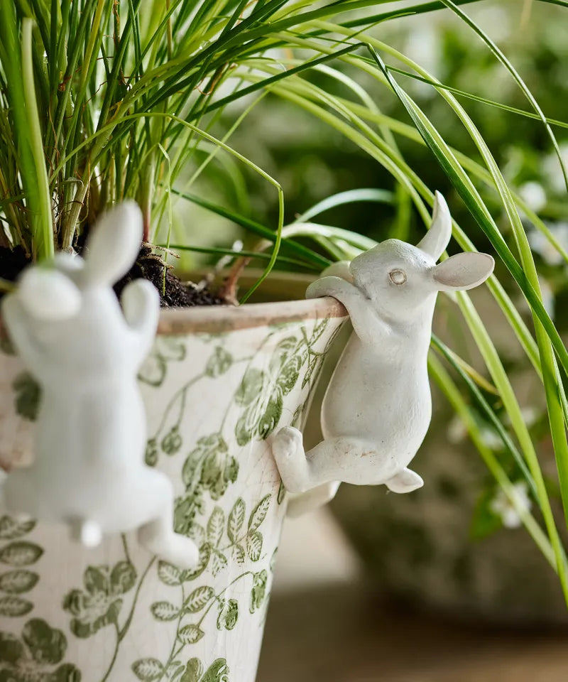 Decorative rabbit-shaped plant holders on a floral-patterned pot with green plants in the background.