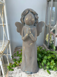 Bronze angel statue with green plants in the background. Angel Statue Rustic praying