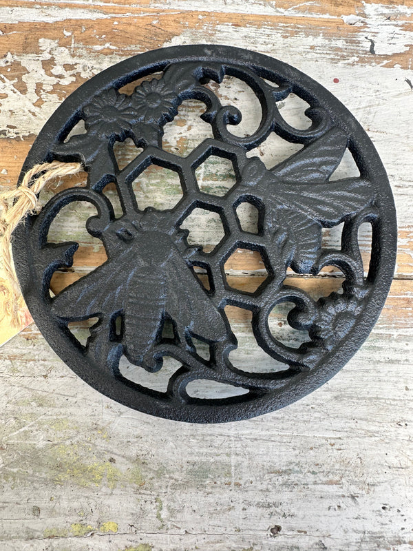 A black cast iron trivet with bee and honeycomb patterns, displayed on a wooden surface.