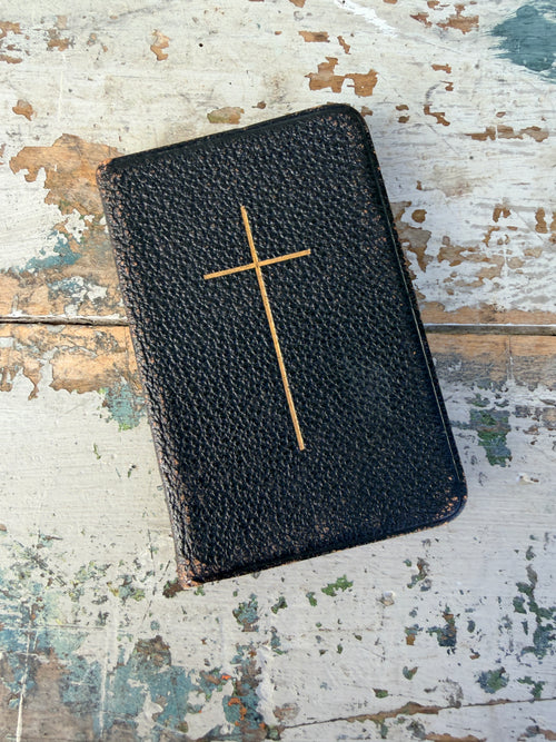 Black leather-bound book with a gold cross on a textured wooden surface