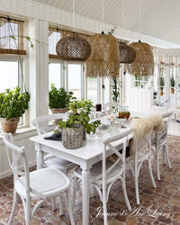 Dining room with white furniture, plants, and woven pendant lights. Issue 6 2025 Jeanne d'Arc Living Magazine