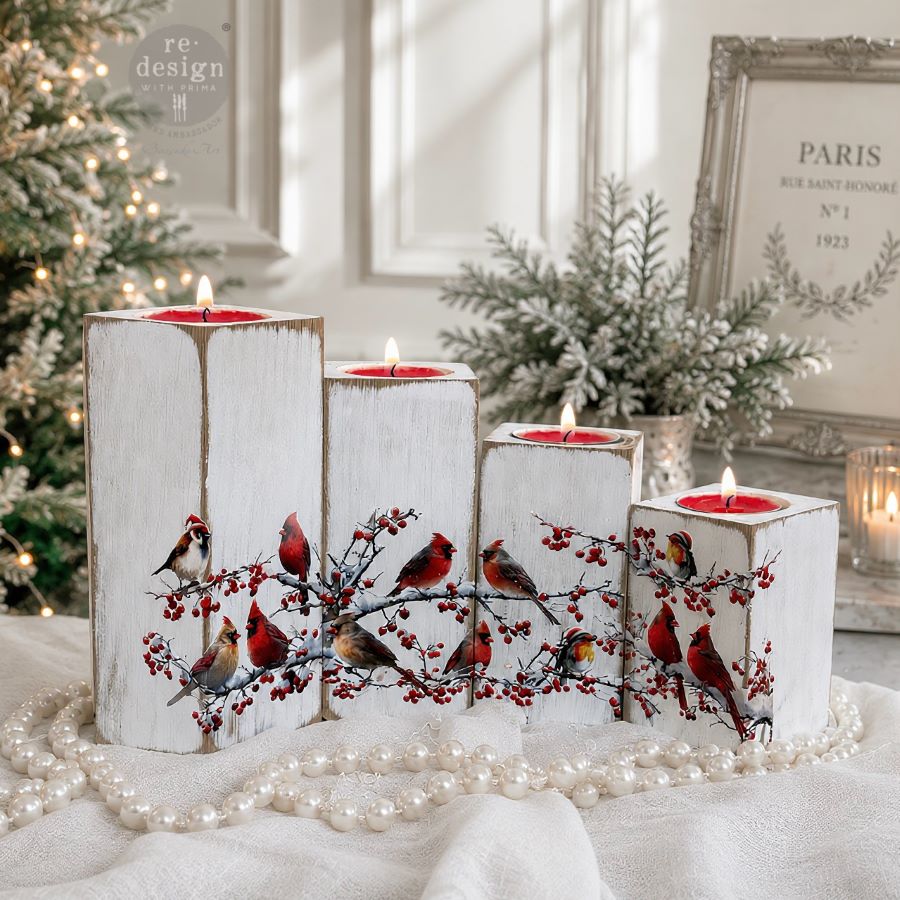 Decorative candles with bird and berry design on a white surface with Christmas decorations in the background. Decorative design of cardinals and berries.  Luxe Transfer Hollywing Cardinal. redesign with Prima Christmas