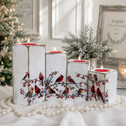 Decorative candles with bird and berry design on a white surface with Christmas decorations in the background. Decorative design of cardinals and berries.  Luxe Transfer Hollywing Cardinal. redesign with Prima Christmas