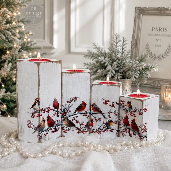 Decorative candles with bird and berry design on a white surface with Christmas decorations in the background. Decorative design of cardinals and berries.  Luxe Transfer Hollywing Cardinal. redesign with Prima Christmas