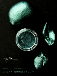 Jar of metallic powder with greenish-brown stones on a black background, featuring 'The Artisan Company' branding. Milan Moonshadow