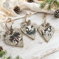 Heart-shaped Christmas ornaments with animal designs on a rustic wooden surface with pinecones and greenery. Redesign with Prima transfer middy Rustic Noel
