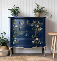 Redesign transfer Large Aviary Elegance Decorative blue dresser with floral and bird designs in a room with plants and a stool.