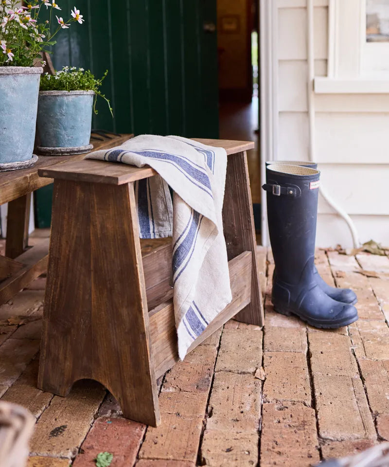 Wooden bench with a towel and blue rubber boot on a brick patio