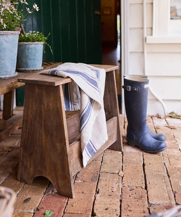 Wooden bench with a towel and blue rubber boot on a brick patio