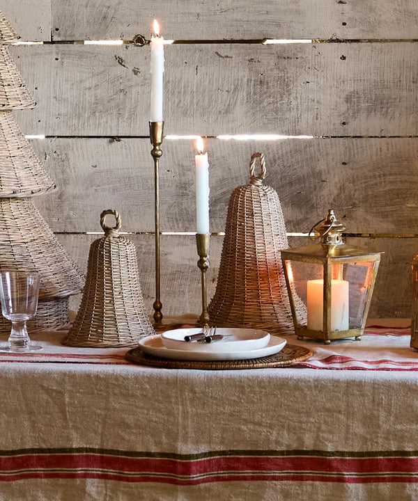 Decorative table setting with candles, wicker lanterns, and striped tablecloth against a wooden wall. French Country Willow Bell Small christmas