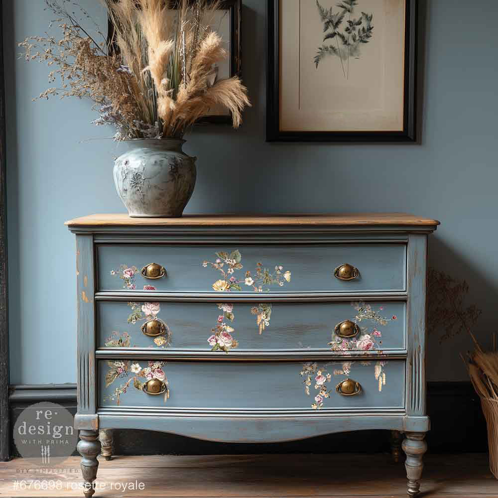 Redesign with Prima transfer middy Rosette Royale Blue dresser with floral designs and gold handles against a blue wall.