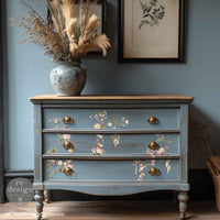 Redesign with Prima transfer middy Rosette Royale Blue dresser with floral designs and gold handles against a blue wall.