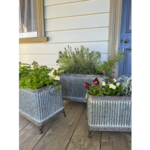 Three galvanized metal planter boxes with a ribbed tin texture, displayed on a wooden porch. v