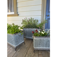 Three galvanized metal planter boxes with a ribbed tin texture, displayed on a wooden porch. v